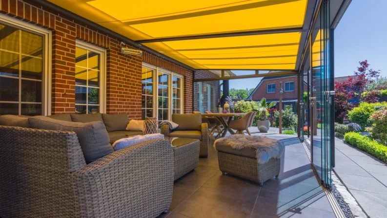 Covered outdoor seating area with wicker sofas and a dining table on a patio under a yellow canopy.